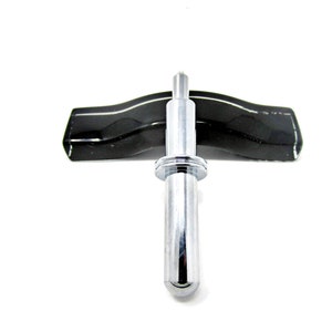 May include: A silver-colored metal tool with a pointed tip and a ring around the middle. The tool is resting on a black, curved surface.