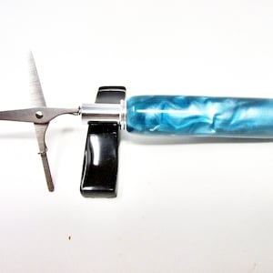May include: A teal and white marbled pen with a silver cap and a small pair of scissors attached to the end.