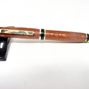 May include: A wooden pen with a gold band and black accents. The pen has a brown wood grain pattern.