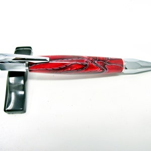 Könnte beinhalten: Ein roter und schwarzer, wirbelförmiger Stift mit silbernem Metallclip und Spitze.