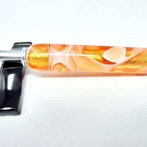 May include: A close-up of a pen with a peach and white marbled body and a silver metal tip. The pen is lying on a black surface.