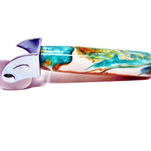 May include: A pizza cutter with a decorative handle. The handle features a swirling pattern of white, teal, orange, and brown. The cutting wheel is a light purple color, and the metal components are silver.