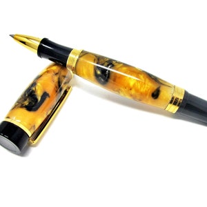 Op de afbeelding: Een zwarte en gouden rollerball pen met een geel en zwart marmerpatroon. De pen is gesloten en ligt op een wit oppervlak.