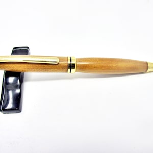 May include: A wooden pen with a gold-toned clip and tip. The pen is made of a light brown wood and has a black band around the middle.