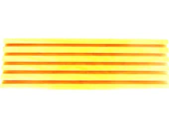 Puede incluir: Una pila de listones de madera amarillos y naranjas. Los listones son rectangulares y tienen una superficie lisa. El color naranja es visible entre los listones amarillos. El fondo es blanco.