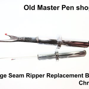 May include: Chrome-plated seam ripper replacement blade. The blade is sharp and pointed, with a small red dot at the tip. The blade is attached to a metal handle.