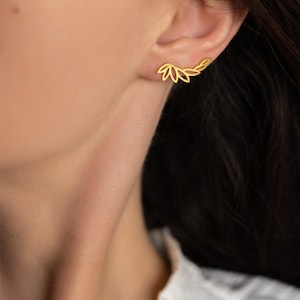 Op de afbeelding: Een goudkleurige ear climber-oorbel met een reeks onderling verbonden, opengewerkte blad- of bloemblaadjesvormen die de welving van de oorlel volgen. Het metaal heeft een gladde, gepolijste afwerking en een heldere geelgouden kleur.