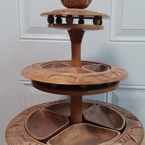 May include: A three-tiered wooden serving tray with carved details. The top tier has a small, carved bowl, while the lower two tiers each have four smaller bowls.