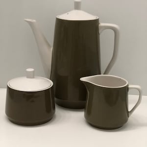 May include: A brown and white ceramic coffee pot, creamer and sugar bowl set. The coffee pot has a white lid and a brown body. The creamer and sugar bowl have white lids and brown bodies.