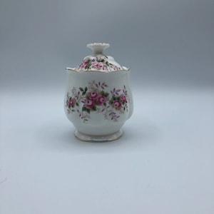 Peut inclure: Sucrier en porcelaine blanche avec un couvercle, orné d'un motif floral de roses roses et de feuilles vertes. Le couvercle est doté d'une bordure dorée et d'un petit bouton.