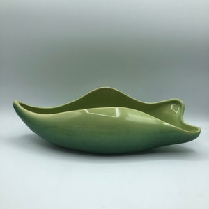 May include: A green ceramic bowl with a unique, organic shape. The bowl is glazed with a light green colour that fades to a darker green at the bottom.