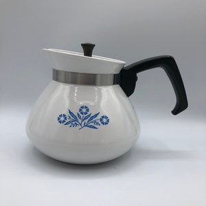 May include: White enamel teapot with a black handle and a blue floral design. The teapot has a silver band around the top.