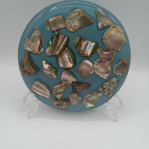 May include: A round, blue coaster with a decorative design of iridescent shell pieces embedded in the surface.