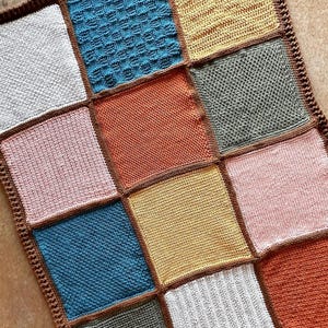 May include: A crocheted blanket with a patchwork design featuring squares in various colours, including white, pink, blue, yellow, orange, and brown.