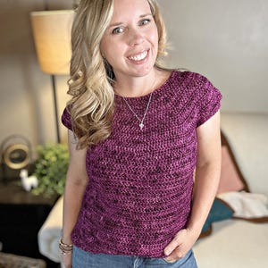 May include: A magenta crochet top with short sleeves. The top has a textured appearance and is worn with blue jeans. The website "hookedonhomemadehappiness.com" is visible in the bottom left corner.