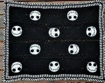 May include: Black and white crochet blanket with a repeating pattern of Jack Skellington's face. The blanket has a white and black border.