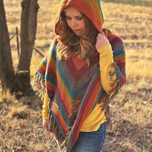 May include: A colorful, hooded poncho with a fringed hem. The crochet poncho features a vibrant array of colors, including blue, orange, yellow, and red. The text "hookedonhomemadehappiness.com" is visible at the bottom of the image.