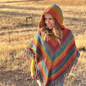 May include: A colorful, hooded crochet poncho with a fringed hem. The poncho features a striped pattern in shades of orange, yellow, teal, and burgundy. The text "hookedonhomemadehappiness.com" is visible at the bottom of the image.