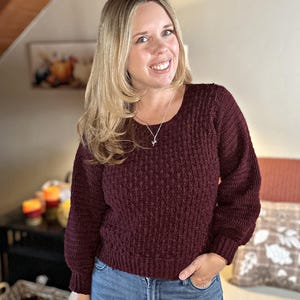 May include: A burgundy-coloured, textured crochet sweater with a crew neck and long sleeves. The sweater is paired with blue jeans. The image includes the text "hookedonhomemadehappiness".