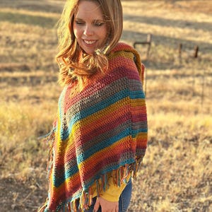 May include: A colorful, handmade crochet poncho with a hood and fringe. The poncho features stripes of red, orange, yellow, teal, and brown. The fringe is a mix of colors. The text "hookedonhomemadehappiness.com" is visible.