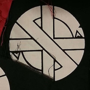 May include: A white patch with a black circle and a diagonal line across it. The circle is divided into four sections, each with a black triangle.