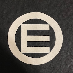 Può includere: Un cerchio bianco con una lettera E bianca al suo interno. Il cerchio e la lettera sono su uno sfondo nero.