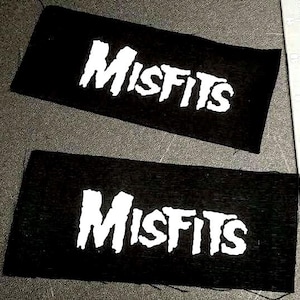 Może przedstawiać: Dwa czarne łatki z tkaniny z nadrukiem "MISFITS" w kolorze białym, w pogrubionym, stylizowanym kroju pisma.