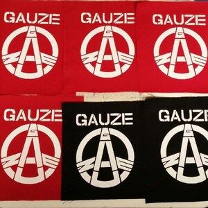 May include: Six fabric patches with the word "GAUZE" and a stylized peace sign with the letter "A" inside. Three patches are red with white lettering and three patches are black with white lettering.