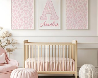 May include: A nursery scene featuring a light wood crib with a pink skirt, a pink armchair, and a round pink ottoman. Above the crib are three framed prints: two with a pink floral pattern and one with the letter "A" and the name "Amelia" in pink.