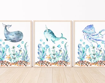 May include: Three watercolor paintings of sea creatures. The first painting features a whale, the second a narwhal, and the third a jellyfish. Each painting has a white background and features blue and green seaweed, orange starfish, and brown rocks.
