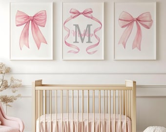 May include: Three framed art prints featuring watercolor illustrations of pink bows. One print includes the letter "M" and the name "Madeline" in gray script. The prints are displayed above a light wood crib with pink bedding.