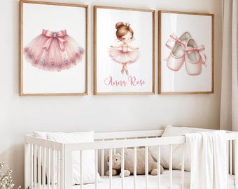 May include: Three framed watercolor prints featuring ballet-themed illustrations. One shows a pink tutu with a bow, another a ballerina with the name "Anna Rose", and the third a pair of ballet shoes with pink ribbons. The prints are displayed above a white crib.