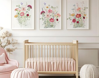 May include: Three framed floral watercolor prints with pink, red, yellow, and purple flowers hang above a light wood crib with a pink skirt. A pink armchair, ottoman, and a woven pouf complete the nursery decor.