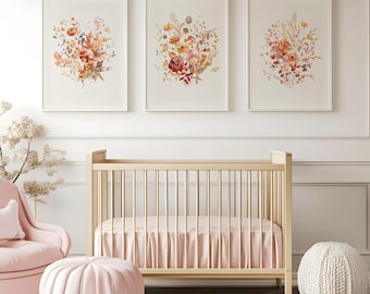 May include: Three framed floral art prints with watercolor bouquets in shades of peach, orange, and brown hang above a light wood crib with a pink skirt. A pink armchair, ottoman, and pouf complete the nursery decor.