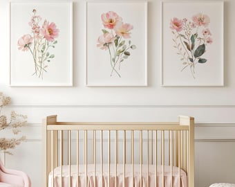 May include: Three framed watercolor prints of pink flowers with green leaves on a white background. The prints are hanging on a white wall above a wooden crib with a pink ruffle crib skirt.