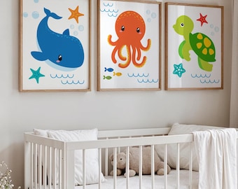 May include: Three framed art prints featuring cartoon sea creatures. A blue whale, an orange octopus, and a green turtle are depicted with starfish, bubbles, and wavy lines. The prints are in wooden frames, suitable for a nursery or children's room.