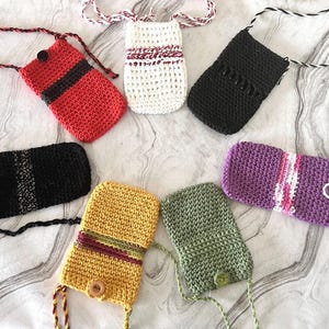 Puede incluir: Una colección de fundas de teléfono de ganchillo hechas a mano en varios colores, incluyendo rojo, negro, blanco, amarillo, verde y morado. Cada funda cuenta con una correa y elementos decorativos únicos como botones y rayas. Estas fundas están diseñadas para guardar un teléfono.