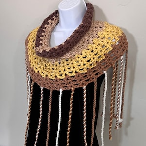 May include: A crocheted cowl with a brown, beige, and yellow color scheme. The cowl has a fringe of brown, white, and beige yarn.