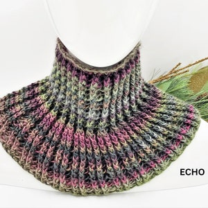 May include: A multi-colored crocheted neck warmer in shades of green, pink, and gray. The neck warmer is displayed on a white mannequin.