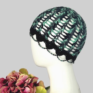 May include: A black and green crocheted beanie with a beaded trim. The beanie is made with a lacy stitch pattern.