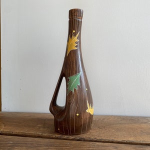 May include: A brown ceramic vase with a unique, elongated shape and a handle-like opening. The vase is decorated with yellow and green leaf designs and small yellow dots. The vase measures approximately 12 inches tall.