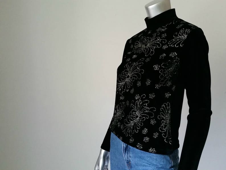 Puede incluir: Top negro de manga larga con cuello alto. La parte superior presenta un intrincado dise&ntilde;o floral plateado en la parte delantera. La modelo lleva vaqueros azules. La parte superior est&aacute; hecha de un material suave y c&oacute;modo.
