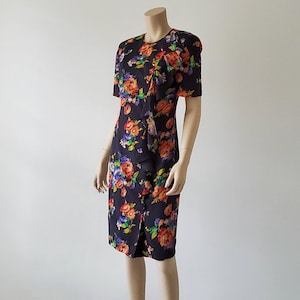 May include: A black dress with a floral print featuring orange, red, purple, and green flowers. The dress has a short sleeve and a fitted silhouette.