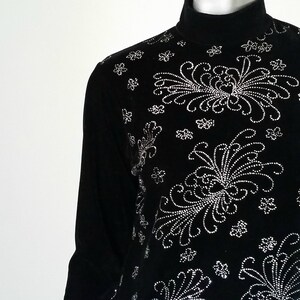 Puede incluir: Camiseta negra de manga larga con cuello alto y dise&ntilde;o floral. El dise&ntilde;o est&aacute; hecho de peque&ntilde;os adornos plateados. La camiseta tiene un cuello alto y una silueta ajustada. El patr&oacute;n floral es sim&eacute;trico y cubre la parte delantera.
