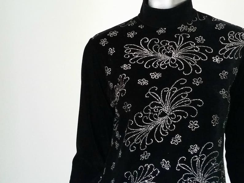 Puede incluir: Camiseta negra de manga larga con cuello alto y dise&ntilde;o floral. El dise&ntilde;o est&aacute; hecho de peque&ntilde;os adornos plateados. La camiseta tiene un cuello alto y una silueta ajustada. El patr&oacute;n floral es sim&eacute;trico y cubre la parte delantera.