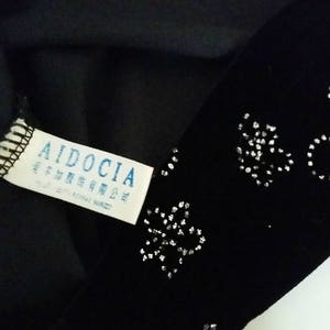 Puede incluir: Tela negra con un patr&oacute;n decorativo plateado. Una etiqueta blanca con la marca "AIDOCIA" y otro texto es visible. La tela parece ser parte de una prenda.