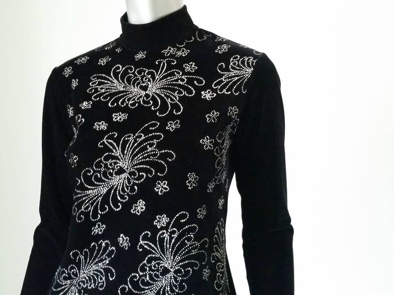 Puede incluir: Top negro de manga larga con cuello alto. El top est&aacute; adornado con un intrincado dise&ntilde;o floral plateado en el pecho y los hombros. El dise&ntilde;o est&aacute; hecho de peque&ntilde;os puntos detallados y l&iacute;neas curvas.