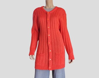 May include: A long-sleeved, bright orange cardigan featuring a vertical ribbed knit pattern, a round neckline, and a front button closure with matching orange buttons. The garment includes two front patch pockets and ribbed cuffs.