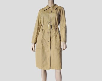 May include: A tan trench coat featuring a classic collar, long sleeves, and a front button closure. The coat includes a matching belt with a rectangular buckle at the waist and two large patch pockets on the front, extending to knee length.