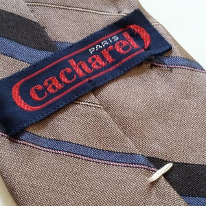 May include: A brown and blue striped tie with a navy blue label that reads "Cacharel Paris" in red lettering.